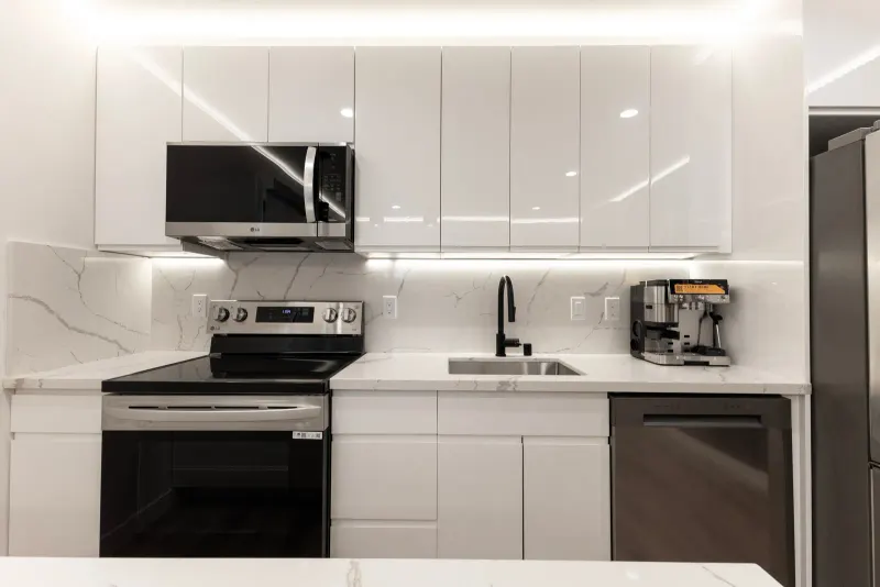 Modern white ADU kitchen with quartz counters, glossy cabinets, and under-cabinet lighting, built by Burton Builders in Berkeley