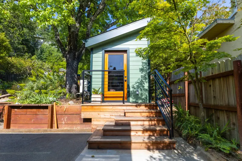 Sage-green detached ADU with a redwood entry deck and steps, built by Burton Builders