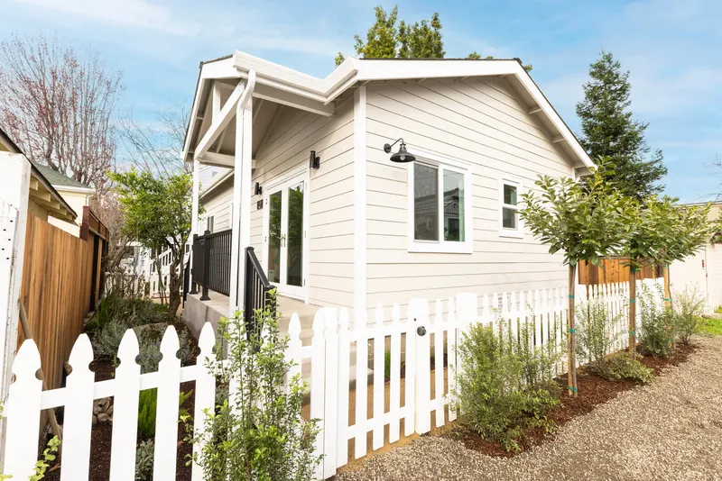 White cottage-style detached ADU with a covered porch and picket fence, built by Burton Builders in San Rafael